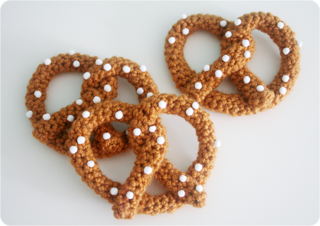 Three crocheted pretzels covered in small white pompom salt.