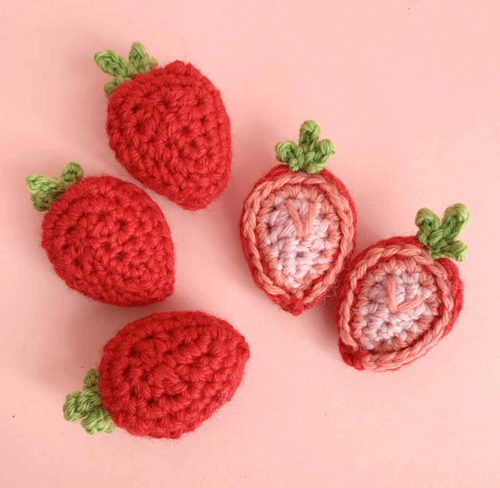 crocheted strawberries and strawberry halves on a pink surface